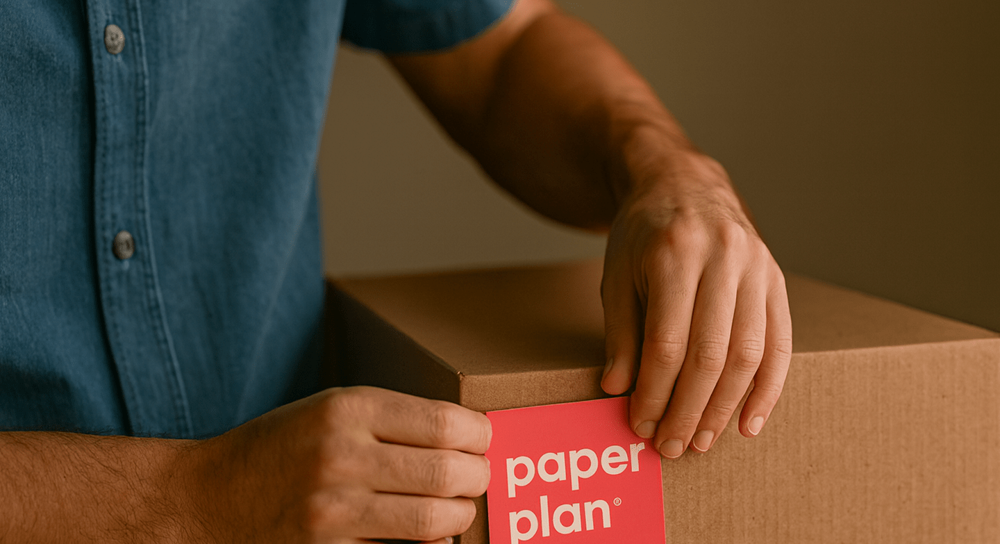 Hands packing a box with a red Paper Plan label